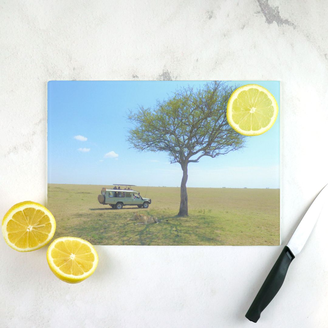 vibrant glass cutting board with a safari vehicle under an acacia tree, surrounded by sliced lemons on a white surface.